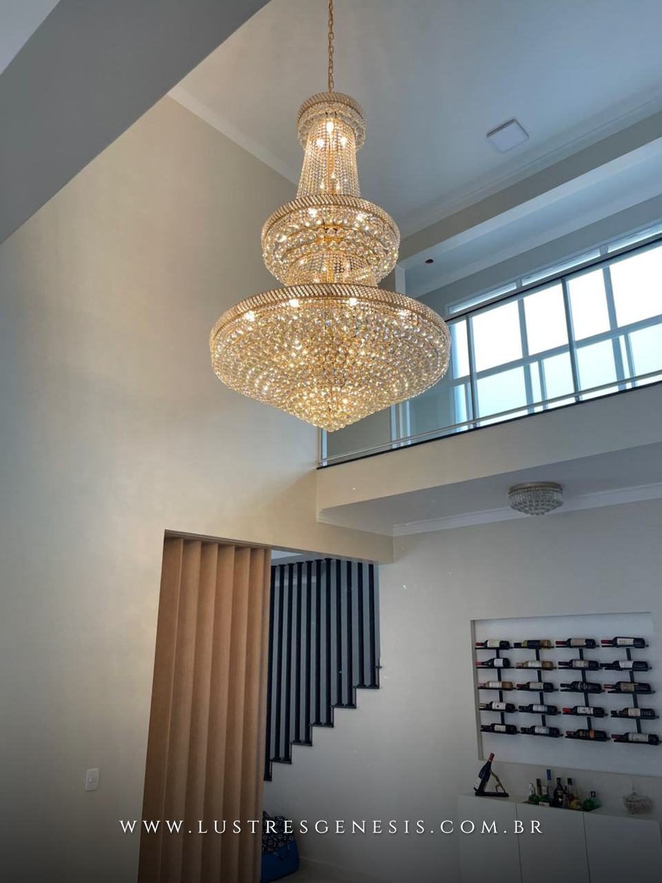 Lustre de cristal cl&aacute;ssico Cant&atilde;o &Oslash;100x170 iluminando sala com p&eacute; direito duplo, destacando eleg&acirc;ncia e sofistica&ccedil;&atilde;o no ambiente residencial.